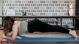 A woman doing plank exercise indoors on a blue mat, promoting fitness and healthy lifestyle.