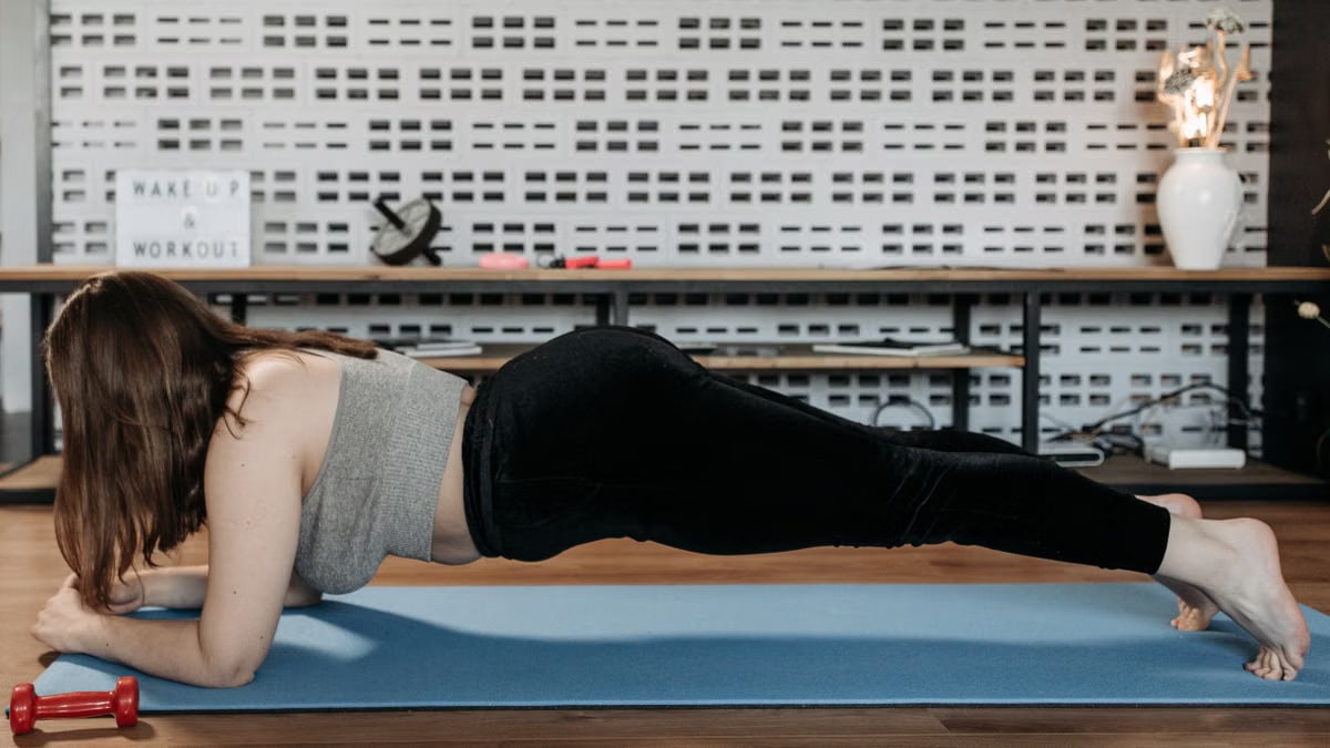 A woman doing plank exercise indoors on a blue mat, promoting fitness and healthy lifestyle.